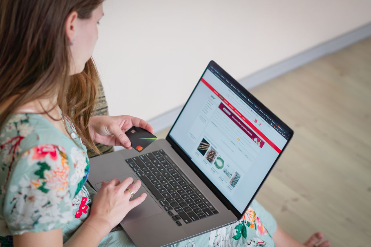 Woman wearing a floral dress shopping online indoors with a laptop and credit card.